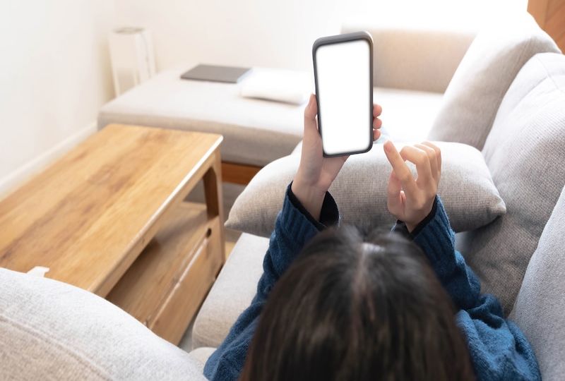 Woman configuring privacy settings on the mobile phone, lying down at home. white screen. "Privacy settings appears on the screen.