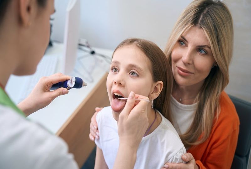 Ear, nose and throat specialist examining throat of little girl