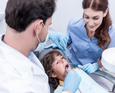 dentists treating teeth of little patient in dentist chair in hospital