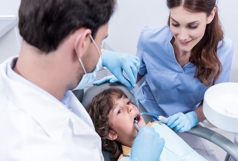 dentists treating teeth of little patient in dentist chair in hospital