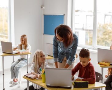 Primary school teacher helping schoolchildren with assignments on a laptop. Education, school concept