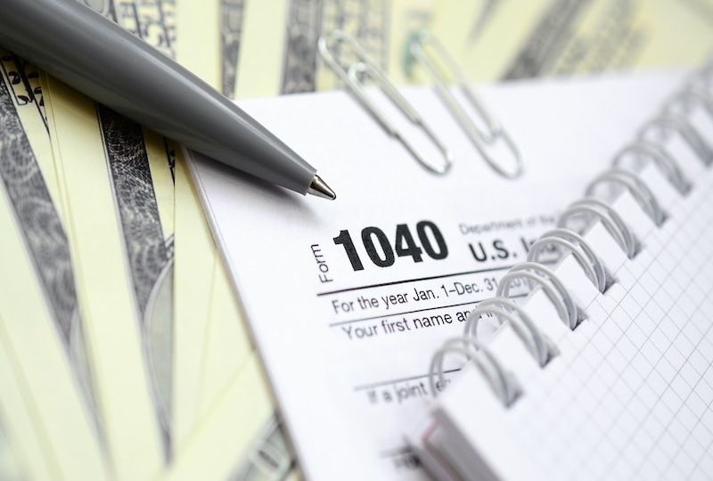 The pen, notebook and dollar bills is lies on the tax form 1040 U.S. Individual Income Tax Return. The time to pay taxes