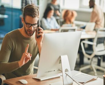 Copy space photo of calm brunette man holding index finger up while having a phonecall at his office desk